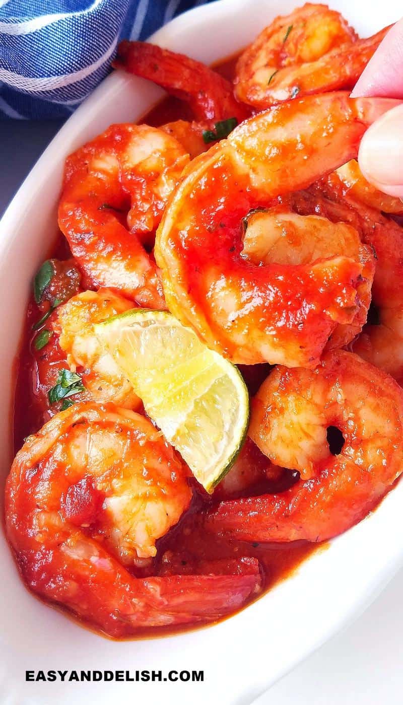 one shrimp a la diabla being held with a hand out of a bowl