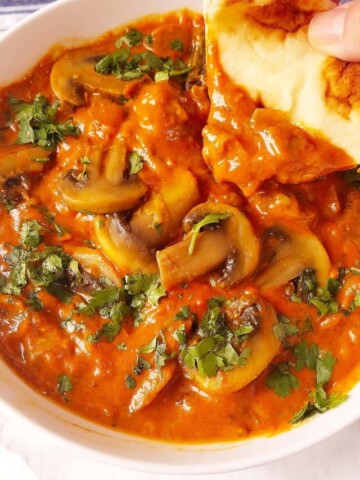 mushroom curry in a bowl with pita being dipped in