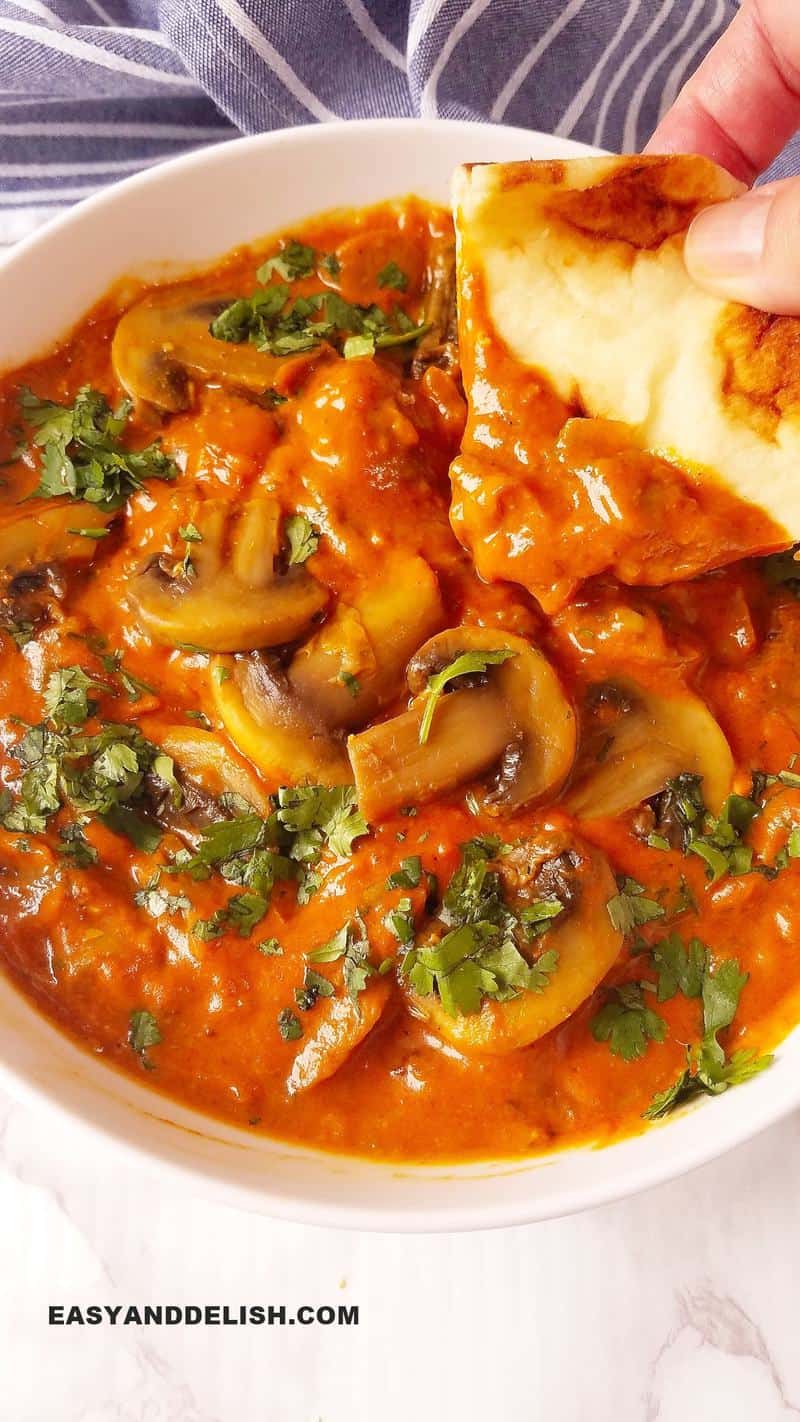 mushroom curry in a bowl witha peice of pita being dipped in