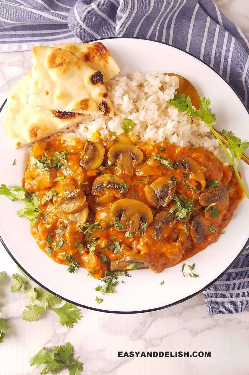 a plate of mushroom curry over rice and with pita on the side