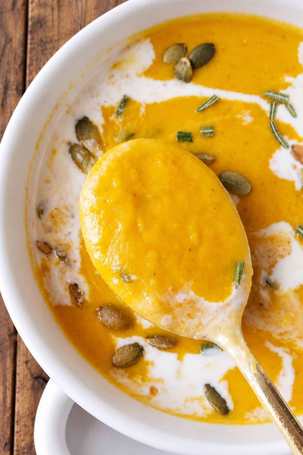 Spoonful of thick orange squash soup lifted from a bowl topped with cream and pepitas.