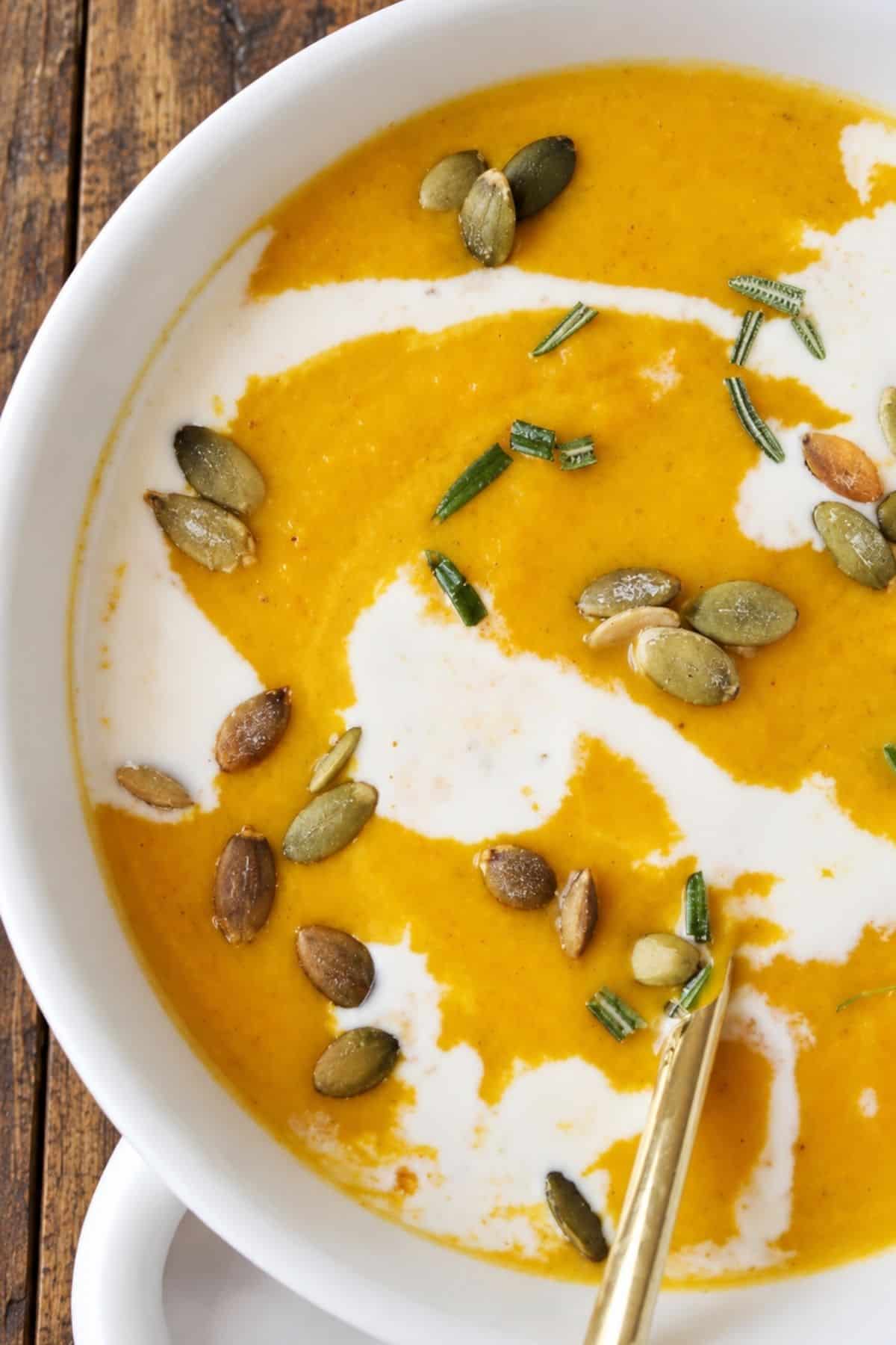Creamy orange squash soup topped with cream, roasted pepitas, and chopped herbs.