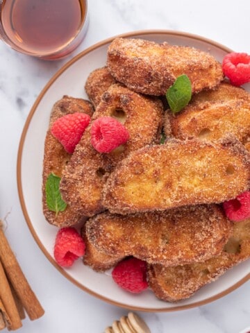 um prato com um monte de rabanada, frutas vermelhas, e mel ao lado