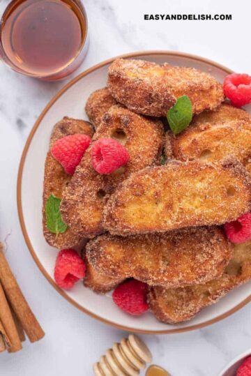 um prato com um monte de rabanada, frutas vermelhas, e mel ao lado