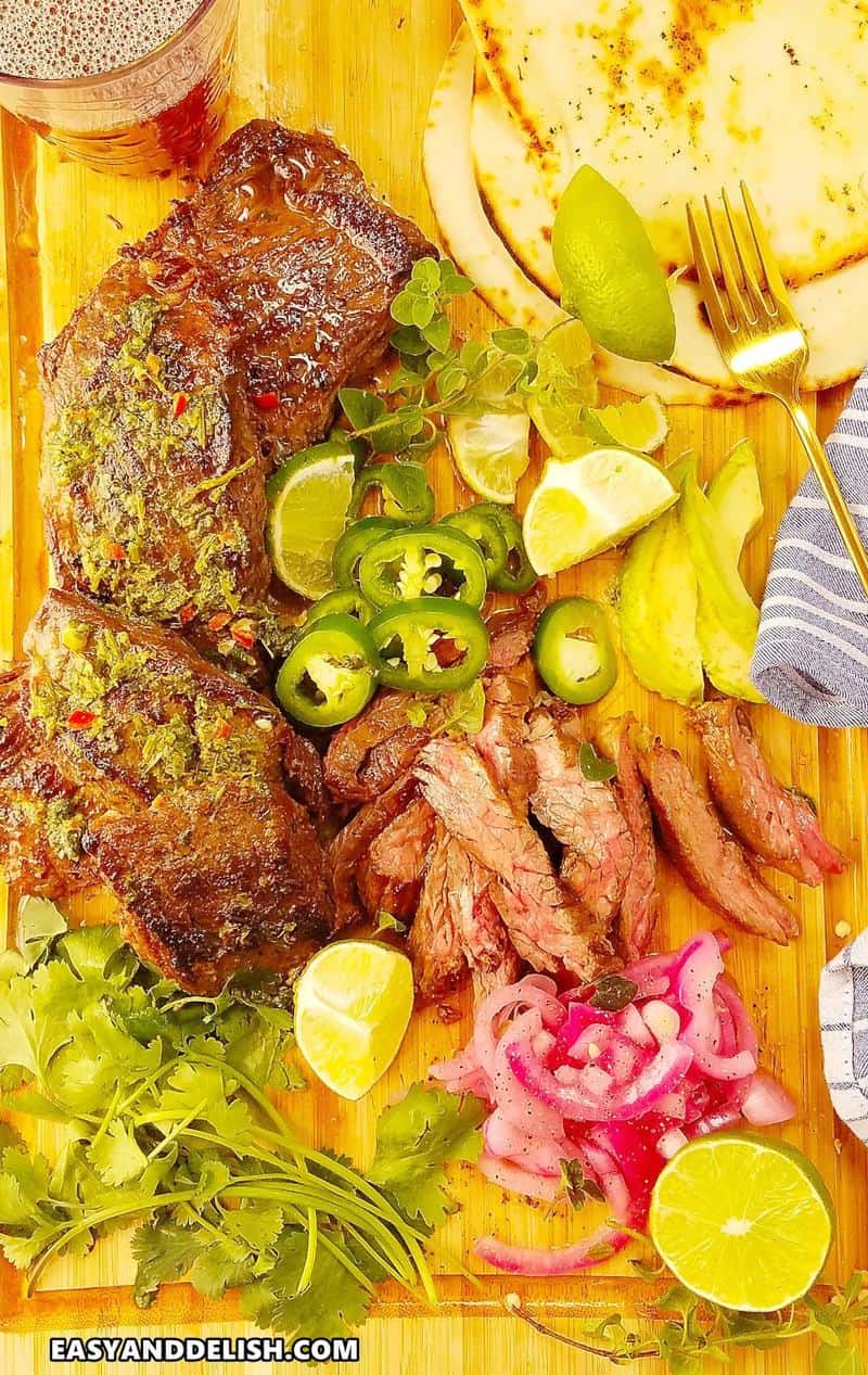 marinated skirt steak with chimichurri sauce and garnishes over a cutting board