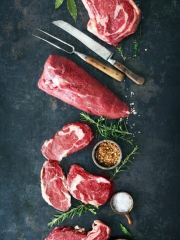 several cuts of beef with spices and herbs on a surface