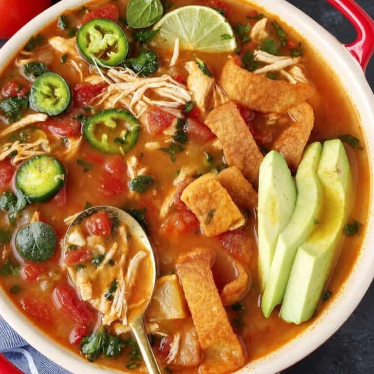 Shredded chicken soup with avocado slices, jalapeño, lime, cilantro, tomatoes, and crisp tortilla strips.