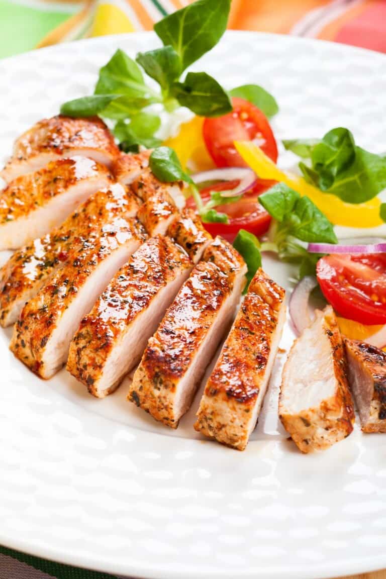 A chicken breast sliced and served with fresh vegetables in a plate.
