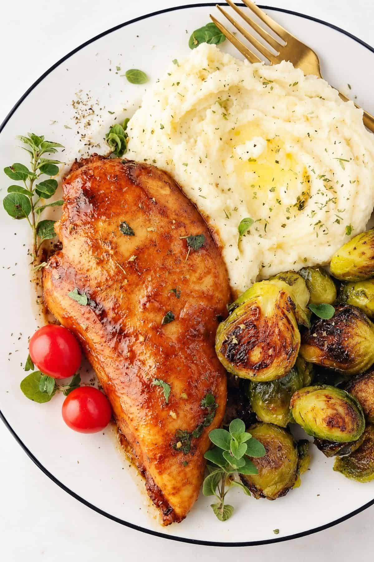 Seasoned chicken breast served with mashed potatoes and roasted Brussels sprouts.