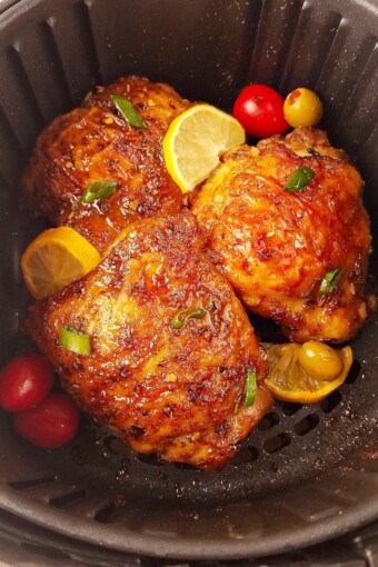 Several chicken thighs in the air fryer with lemon slices.