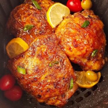 Several chicken thighs in the air fryer with lemon slices.