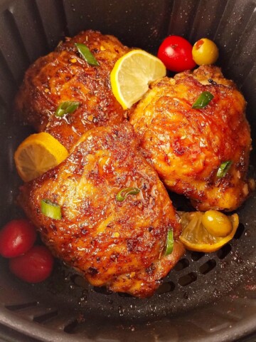 Several chicken thighs in the air fryer with lemon slices.