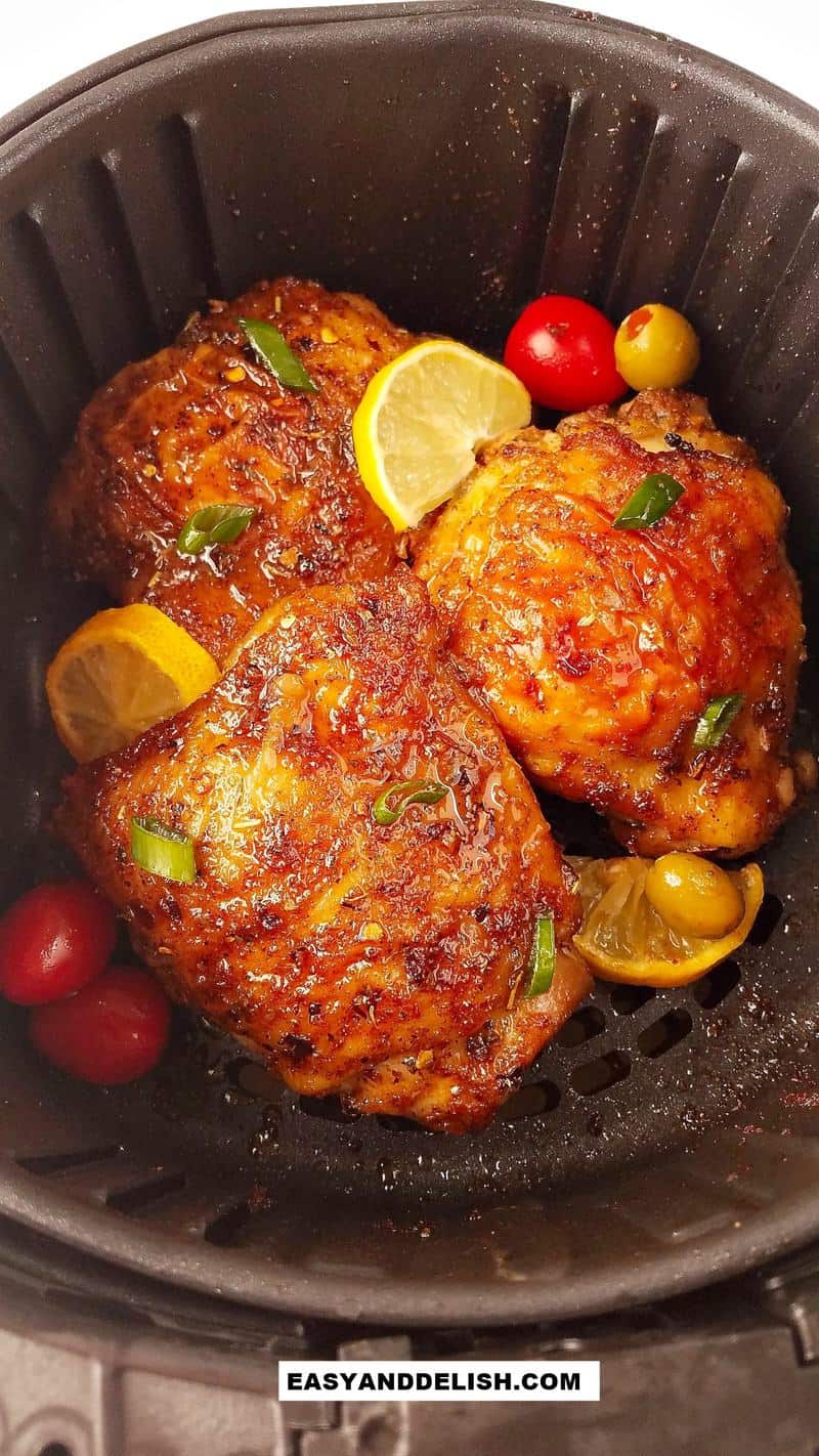 Several chicken thighs in the air fryer with lemon slices.