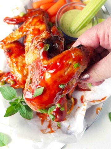 a hand holding a bbq chicken wing cooked in the air fryer