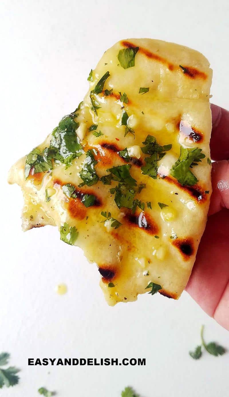 a hand holding a piece of garlic naan