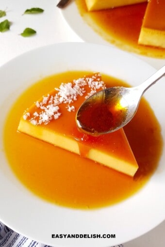 A spoon drizzling caramel over a slice of coconut flan