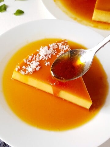 A spoon drizzling caramel over a slice of coconut flan