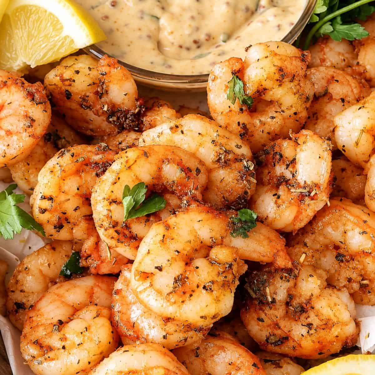 Close-up of air-fried shrimp with visible herbs, lemon wedges, and creamy dipping sauce.
