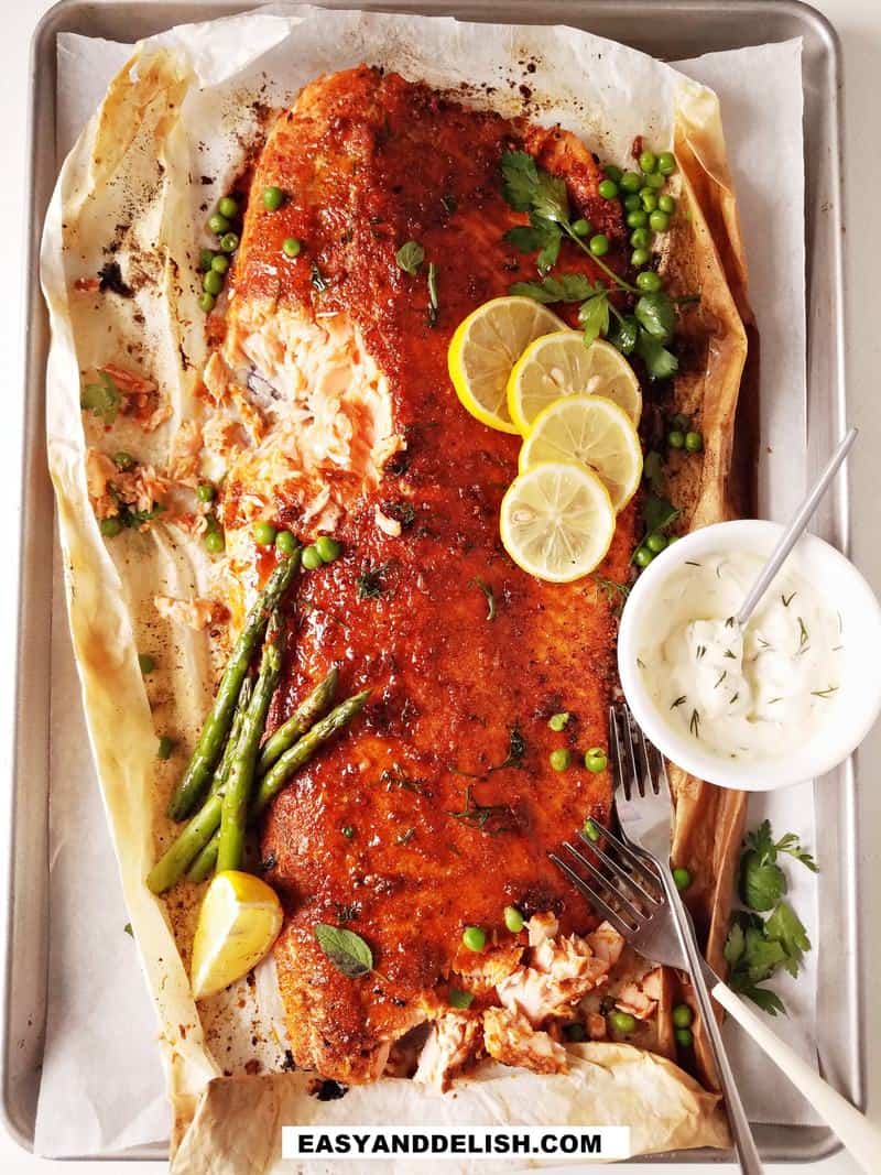 fish on a baking sheet with garnishes and sauce on the side