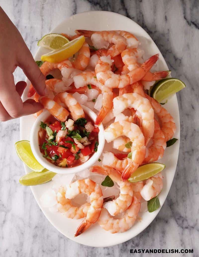 coctel de camarones in a platter and a hand dipping a shrimp into the salsa