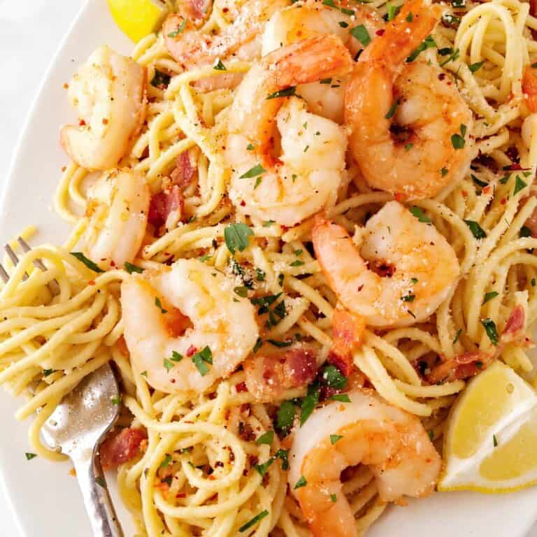 Plated spaghetti with shrimp, bacon, parsley, Parmesan, and lemon wedges.