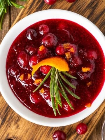 Bowl of chunky cranberry orange sauce garnished with rosemary and orange peel.