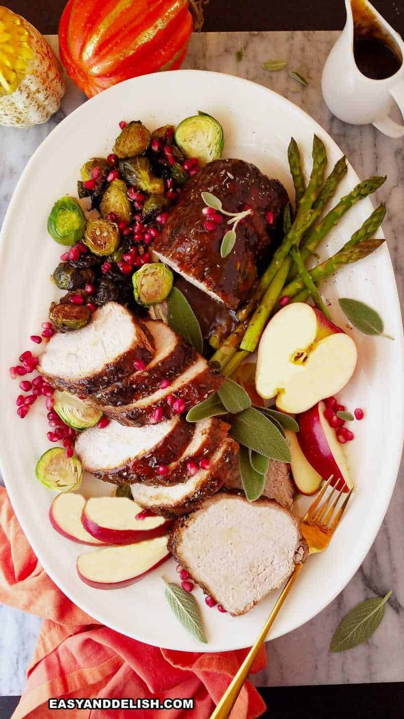 a platter with sliced meat, apples, and cooked vegetables plus sauce on the side 