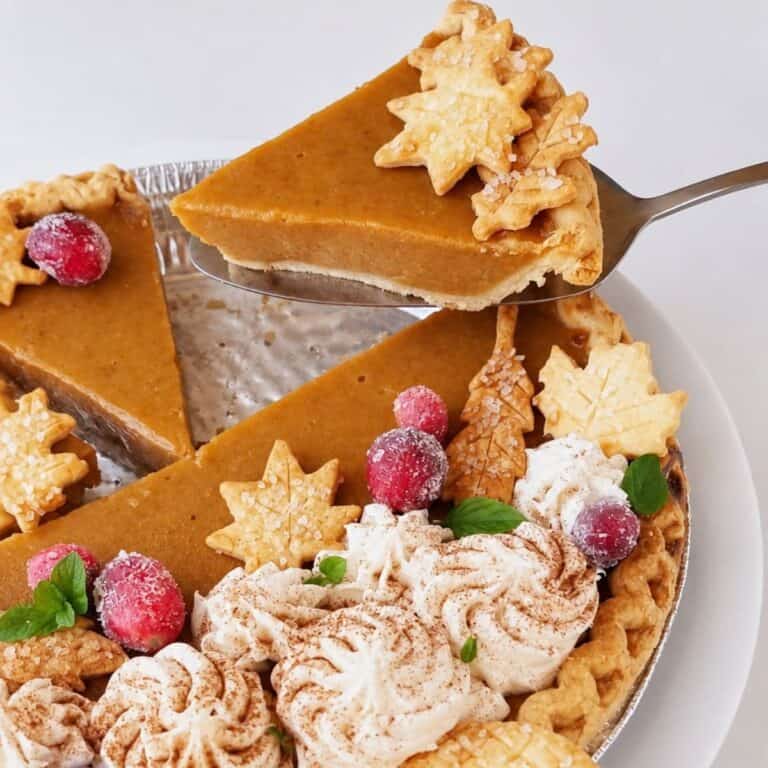 Sweet potato pie slice lifted over the decorated pie with whipped cream, cranberries, and pastry leaves.