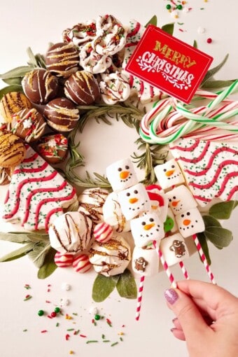 dessert charcuterie board for christmas with a hand holding marshmallows