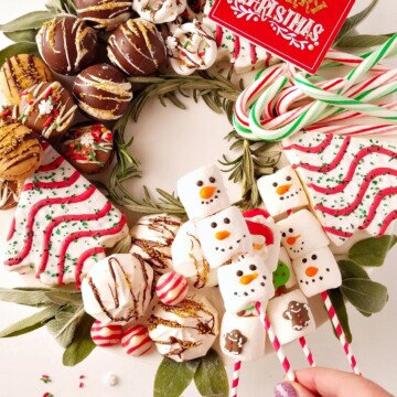 dessert charcuterie board for christmas with a hand holding marshmallows