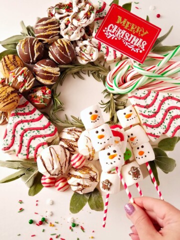 dessert charcuterie board for christmas with a hand holding marshmallows