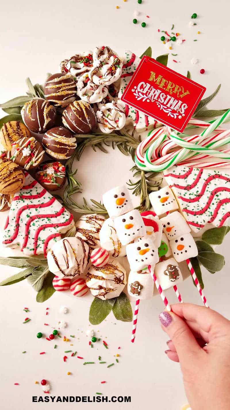 dessert charcuterie board for christmas with a hand holding marshmallows