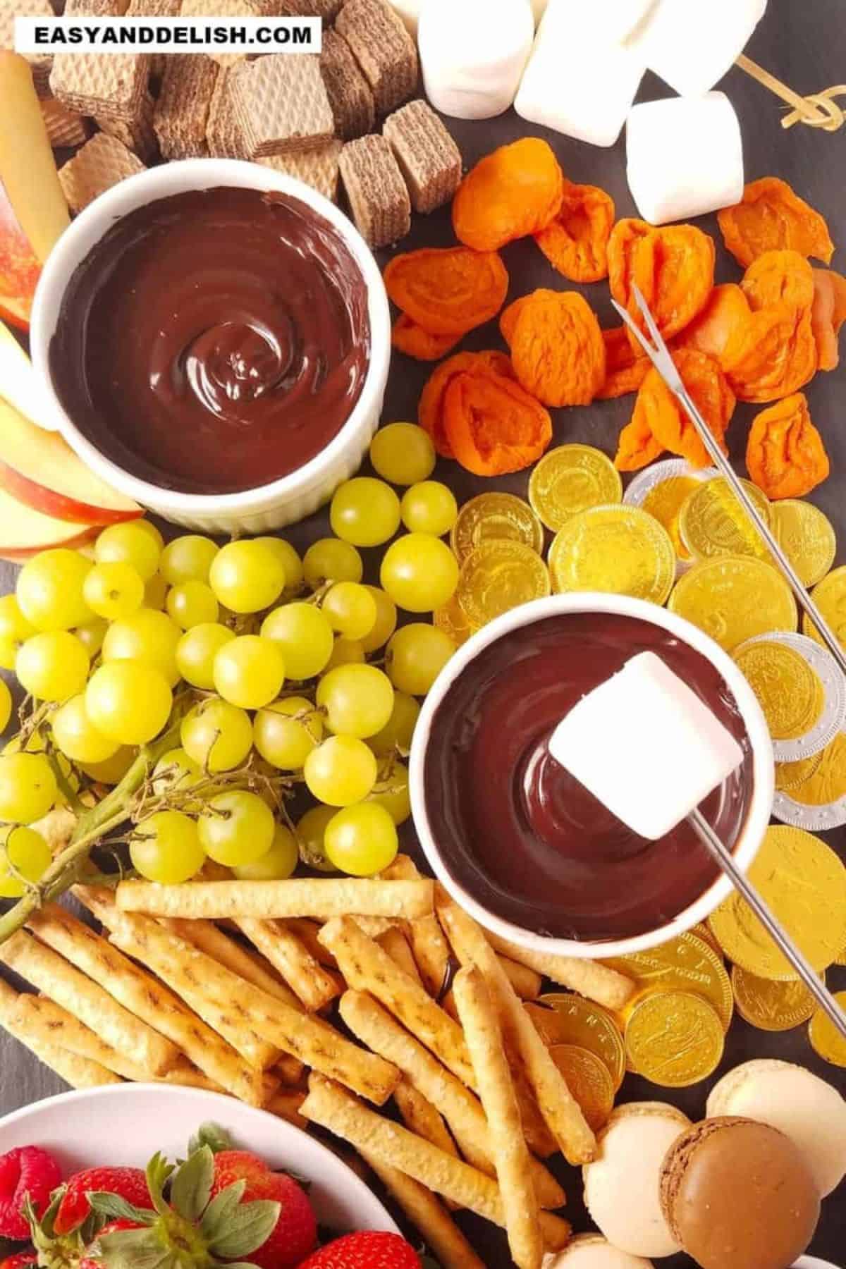 Marshmallow held over melted chocolate with fruit and other dippers.