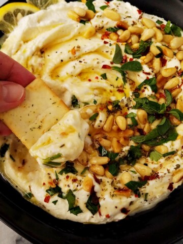 whipped feta dip in a plate and a scoop of it on a pita chip
