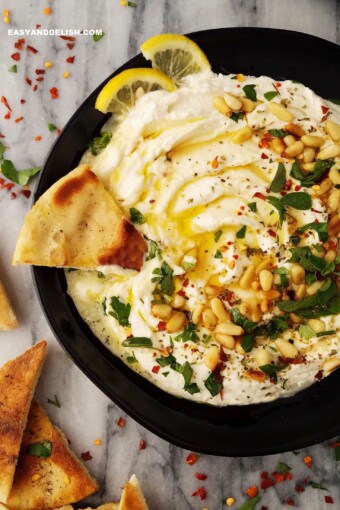a creamy mediterranean spread in a plate with pita chips on the sides