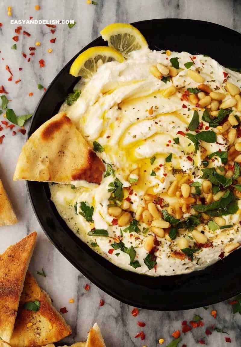 a creamy mediterranean spread in a plate with pita chips on the sides