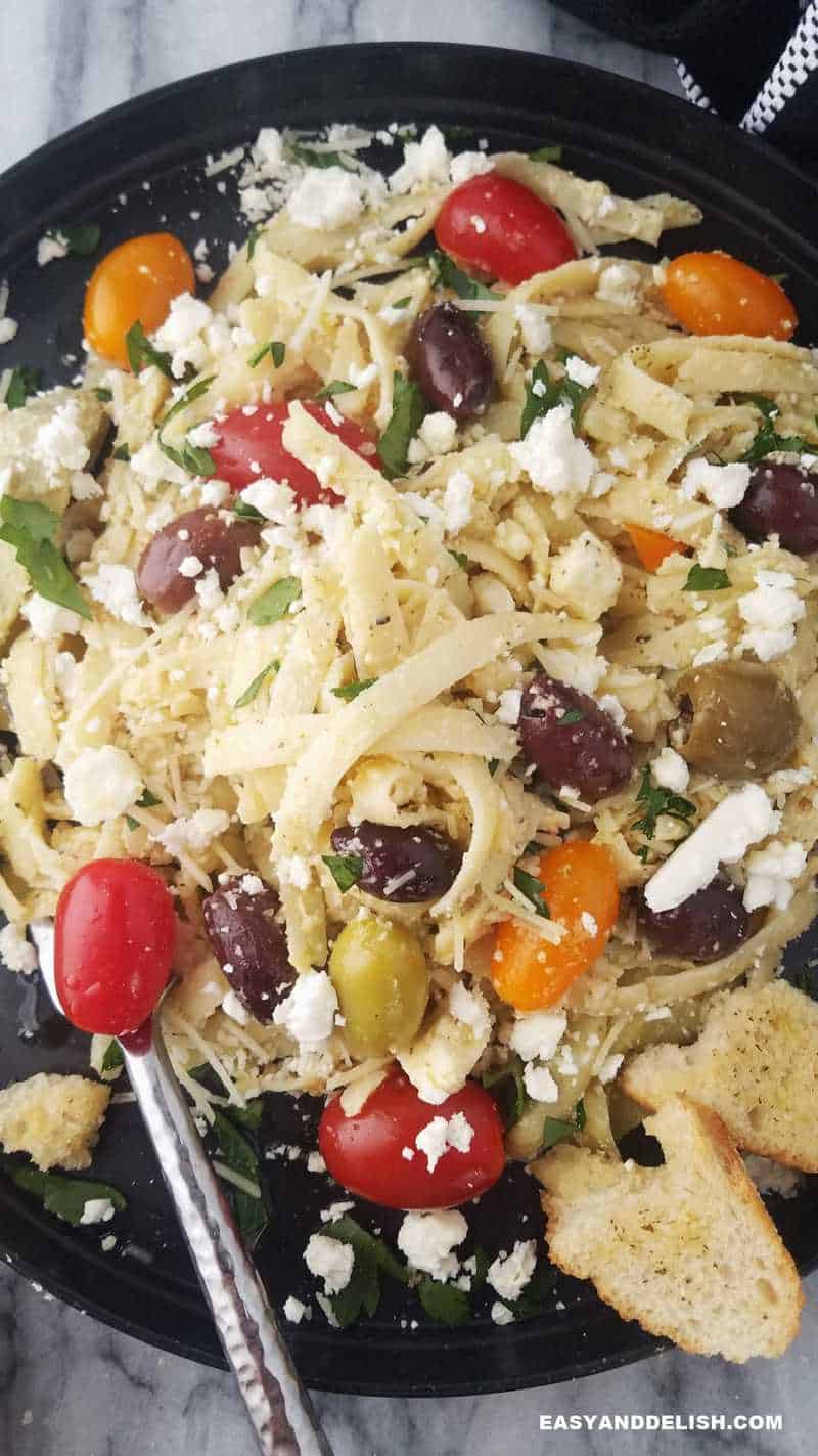 a plate of greek noodles with feta and veggies