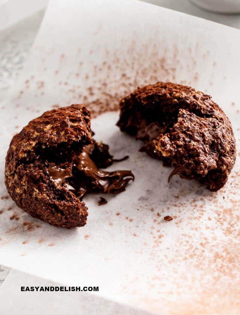 nutella stuffed cookie cut in half over parchment paper and dusted with cocoa powder