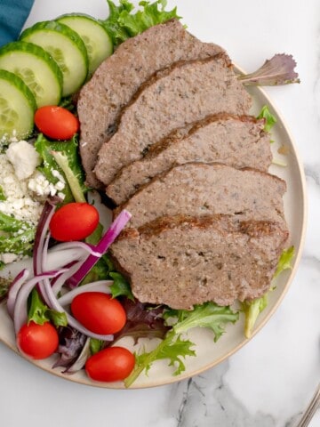 a plate with sliced gyro meat and Greek salad