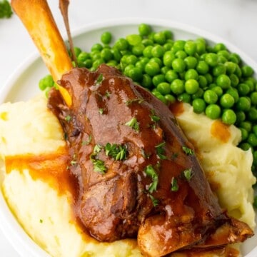 slow cooker lamb shank served over mashed potatoes and with a side of peas