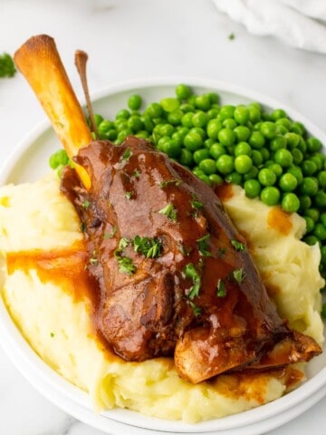 slow cooker lamb shank served over mashed potatoes and with a side of peas