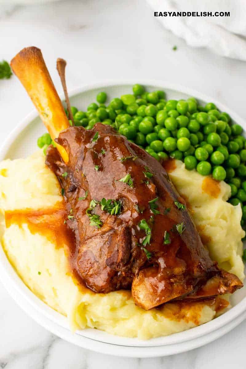 braised lamb shank ser ved over mashed potatoes and with a side of peas