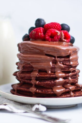 a pile of oat flour pancakes with chocolate and berries
