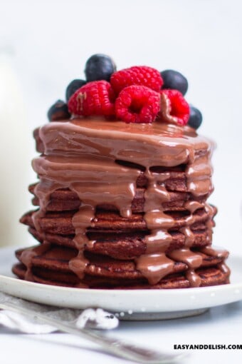 uma pilha alta de panquecas de aveia fit com calda de chocolate e frutas vermelhas por cima