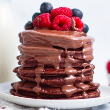 uma pilha alta de panquecas de aveia fit com calda de chocolate e frutas vermelhas por cima