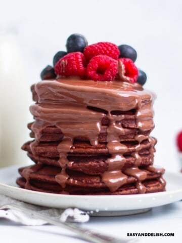 uma pilha alta de panquecas de aveia fit com calda de chocolate e frutas vermelhas por cima