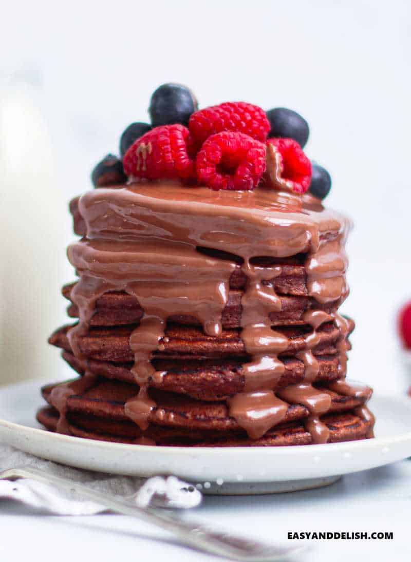 a stack of oat flour pancakes topped with melted chocolate and berries