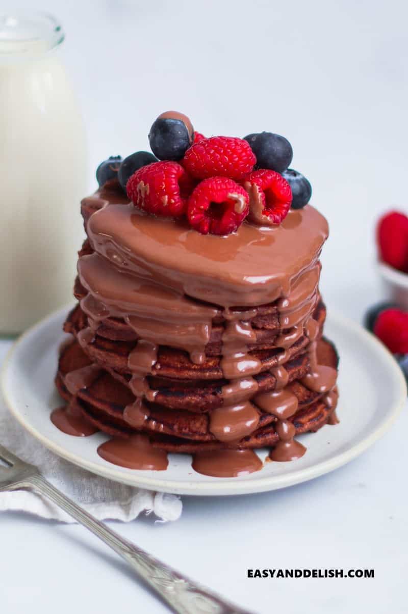 a pile of protein pancakes with melted chocolate and berries