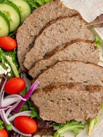 Slices of homemade gyro meat served with cucumber, tomatoes, feta, and mixed greens.