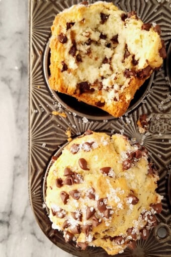 Whole and halved bakery-style chocolate chip muffins in a tin